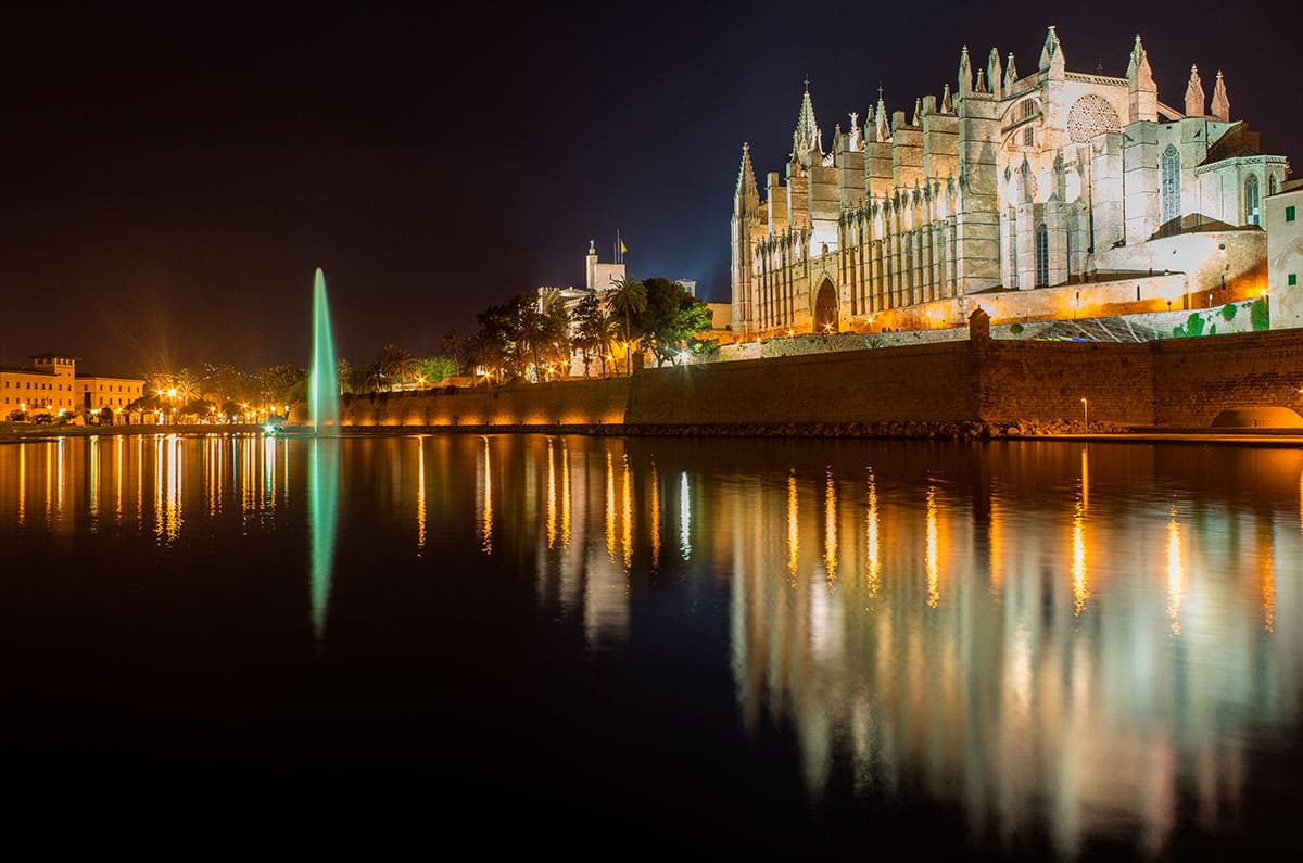 Vista nocturna con la Catedral de Palma iluminada y reflejada en el agua